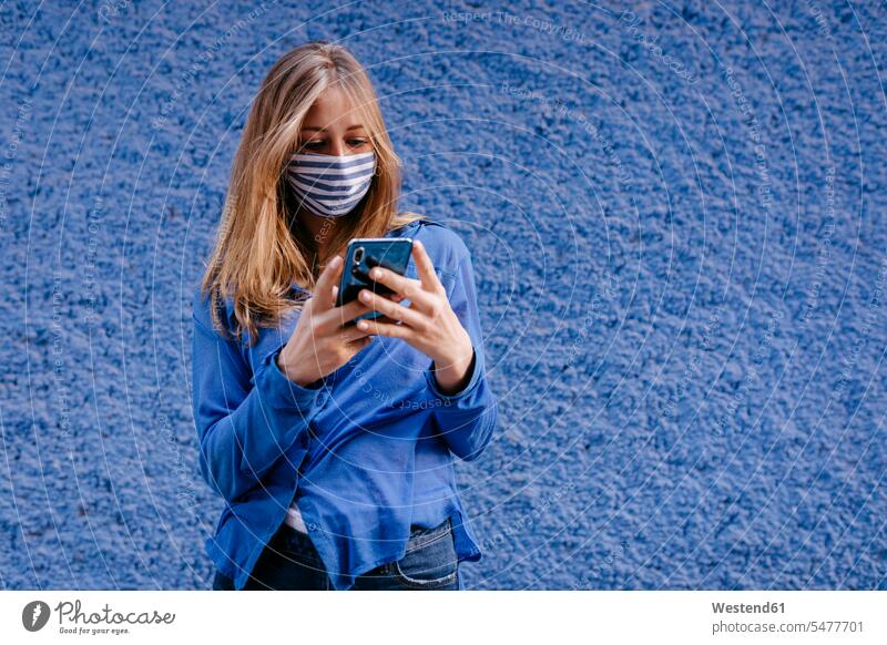 Young woman wearing mask using smart phone while standing against wall in city color image colour image Spain leisure activity leisure activities free time