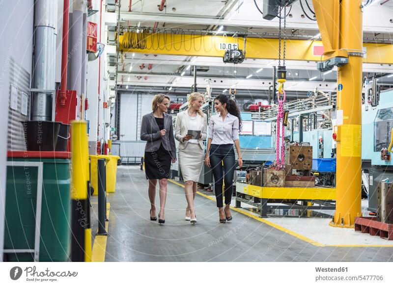 Three women with tablet walking and talking in factory shop floor speaking industrial hall factory hall industrial buildings woman females digitizer