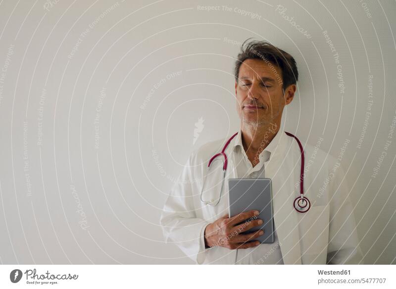 Doctor standing in hospital, using digital tablet doctor physicians doctors Medical Clinic portrait portraits stethoscope doctor's overall lab coat