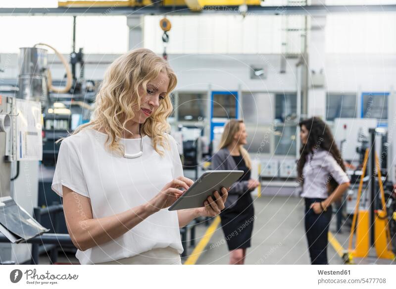 Woman using tablet in factory shop floor with two women in background factories industrial hall factory hall industrial buildings woman females digitizer