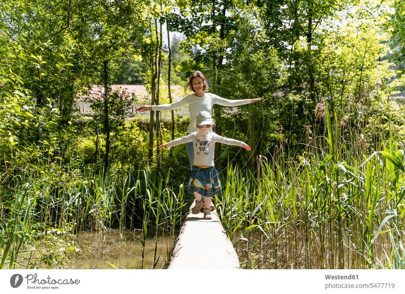 Mother and daughter with arms outstretched walking on footbridge against trees in forest color image colour image Germany leisure activity leisure activities