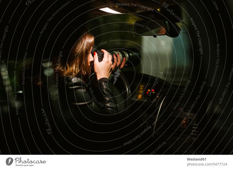 Young woman taking pictures with a camera out of a car at night Occupation Work job jobs profession professional occupation images photo photographs photos