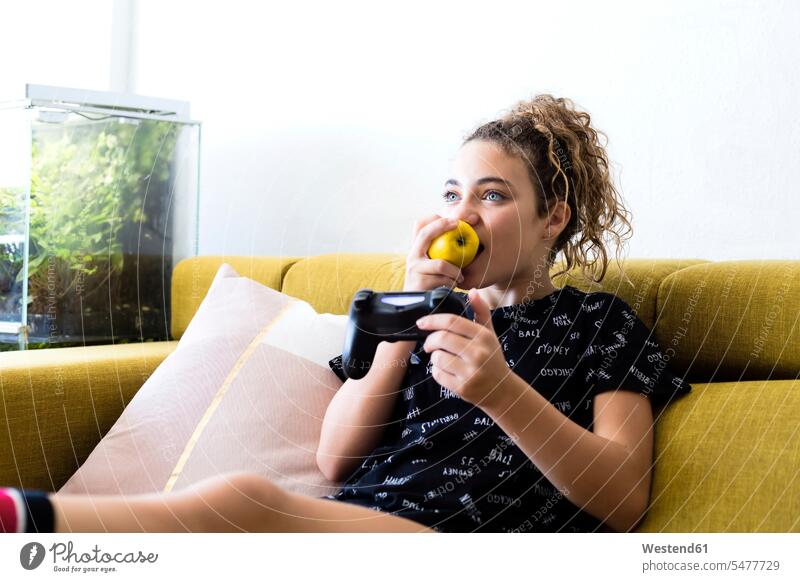 Portrait of girl sitting on the couch at home eating an apple while playing with games consol portrait portraits Apple Apples games console game console