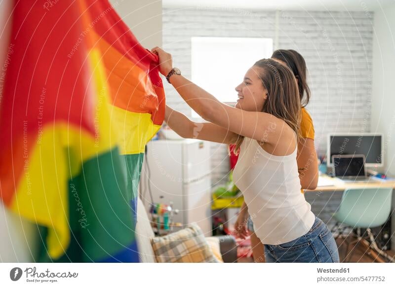 Lesbian couple hanging up rainbow flag at home flags windows banner banners smile delight enjoyment Pleasant pleasure happy Emotions Feeling Feelings Sentiment