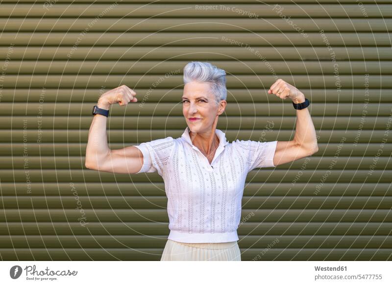 Senior woman flexing muscles while standing against shutter color image colour image outdoors location shots outdoor shot outdoor shots day daylight shot