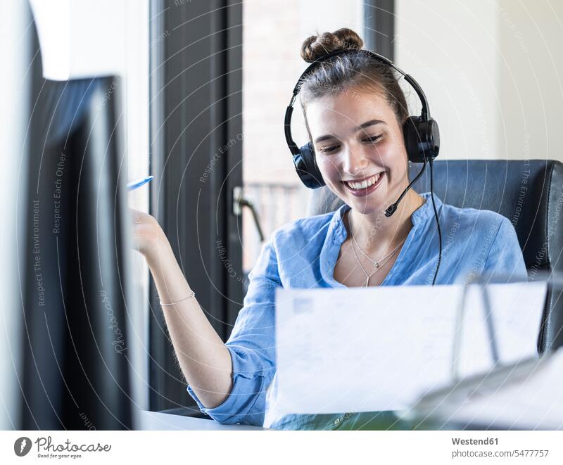 Businesswoman with paper talking through headphones while sitting at office color image colour image indoors indoor shot indoor shots interior interior view