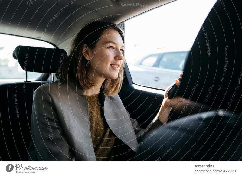 Smiling woman sitting in back seat of a car holding cell phone females women Seated smiling smile backseat mobile phone mobiles mobile phones Cellphone
