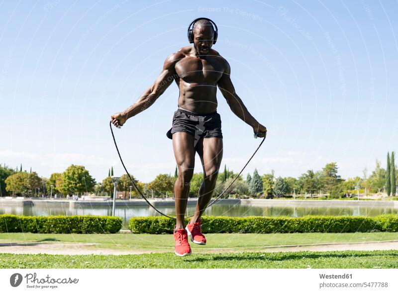 Sportsman doing skipping exercise while listening music through headphones in park on sunny day color image colour image outdoors location shots outdoor shot