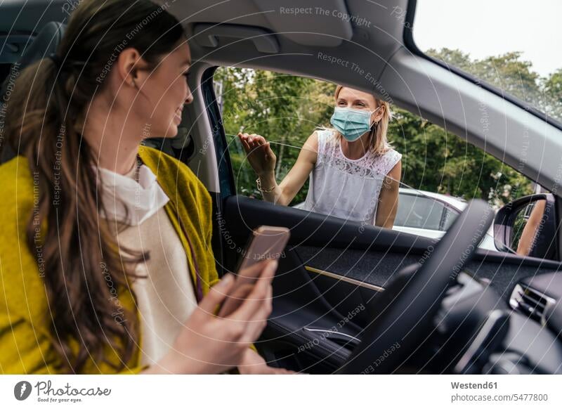 Woman wearing a protective mask talking through car window with woman without mask motor vehicles road vehicle road vehicles Auto automobile Automobiles cars