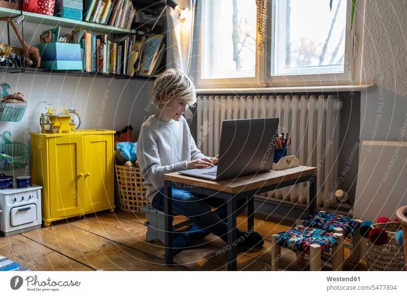Boy using laptop in his room at home windows jumper sweater Sweaters Tables computers Laptop Computer Laptop Computers laptops notebook learn Seated sit play