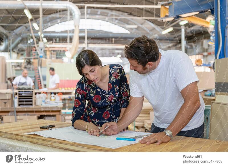 Project manager and architect discussing plan with coworker working in background at factory color image colour image indoors indoor shot indoor shots interior