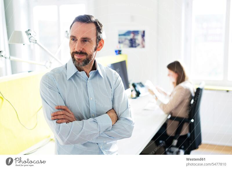 Portrait of confident businessman in office with employee in background Occupation Work job jobs profession professional occupation superior supervisor the boss