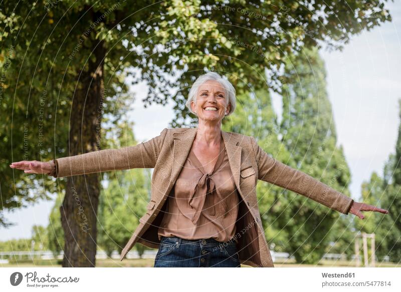 Happy senior woman with outstretched arms in a park senior women elder women elder woman old females parks happiness happy people persons human being humans