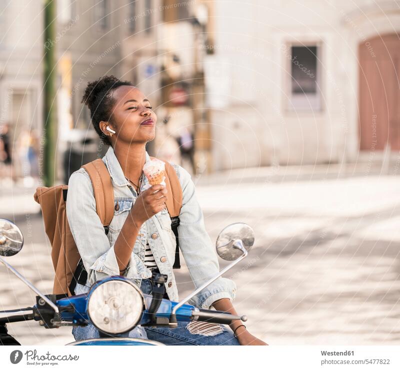 Happy young woman with motor scooter enjoying ice cream in the city, Lisbon, Portugal human human being human beings humans person persons African black