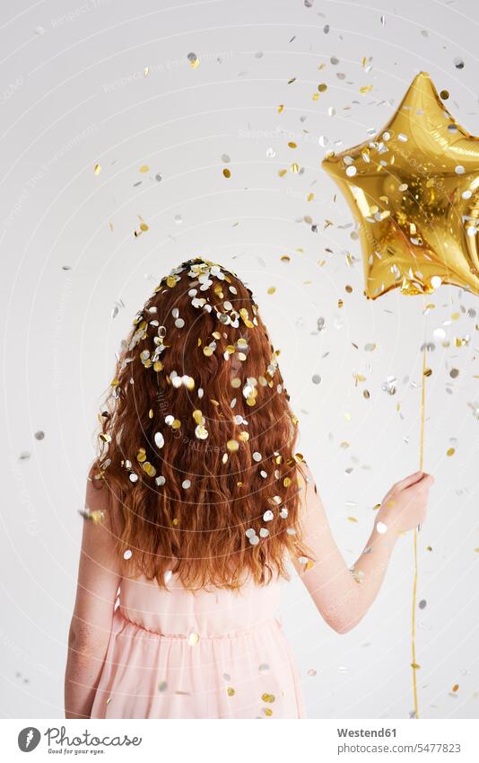 Back view of redheaded young woman with star-shaped golden balloon under shower of confetti balloons Gold Color Gold Colored Star Shape Star Shapes Star Shaped