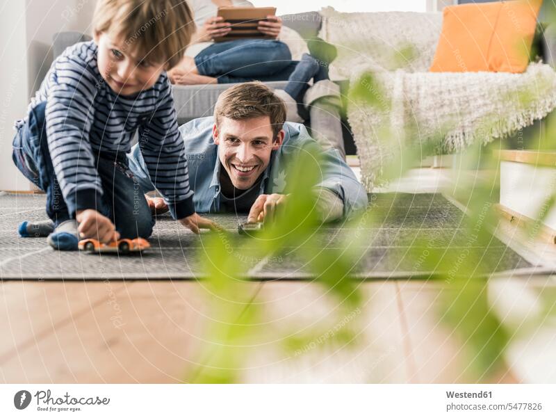Father and son playing with toy cars, lying on floor toys carpets rug rugs smile delight enjoyment Pleasant pleasure happy pleased Auto Racing free time