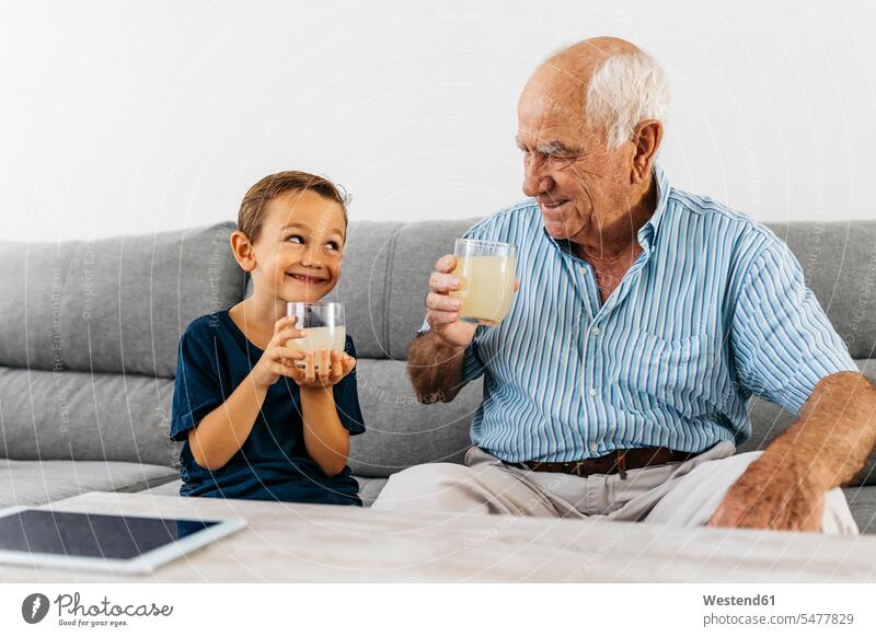 Grandfather and grandson sitting together on couch drinking lemonade settee sofa sofas couches settees Lemonade Seated grandsons grandfather grandpas granddads