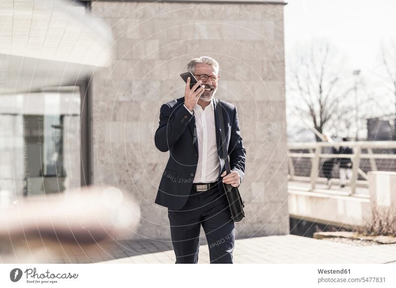 Smiling mature businessman using cell phone outdoors smiling smile on the phone call telephoning On The Telephone calling mobile phone mobiles mobile phones