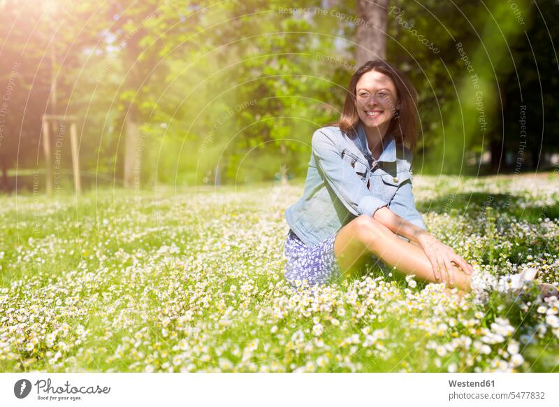 Smiling young woman sitting in a park smiling smile parks females women Seated Adults grown-ups grownups adult people persons human being humans human beings