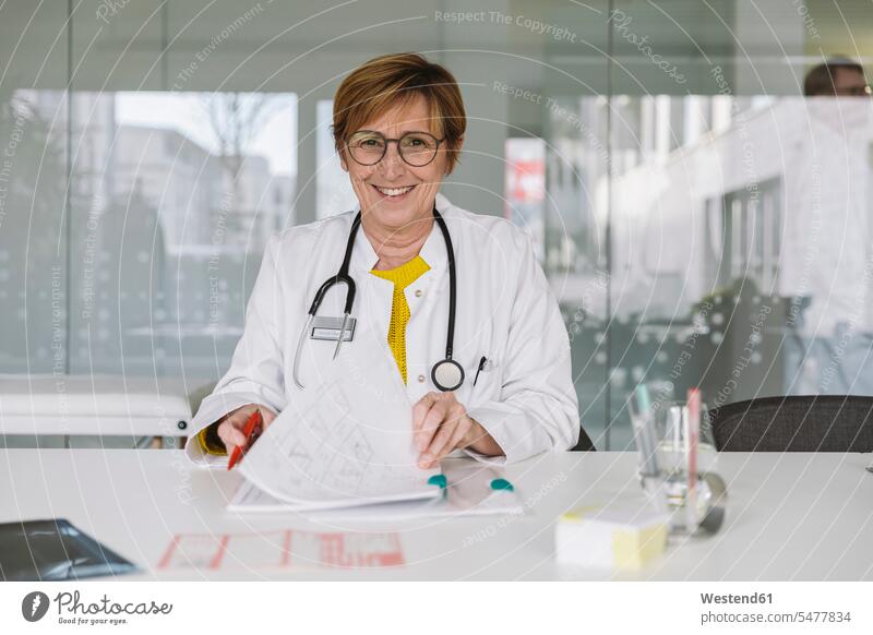 Portrait of smiling doctor sitting at desk Occupation Work job jobs profession professional occupation documents paper papers glass panes health healthcare