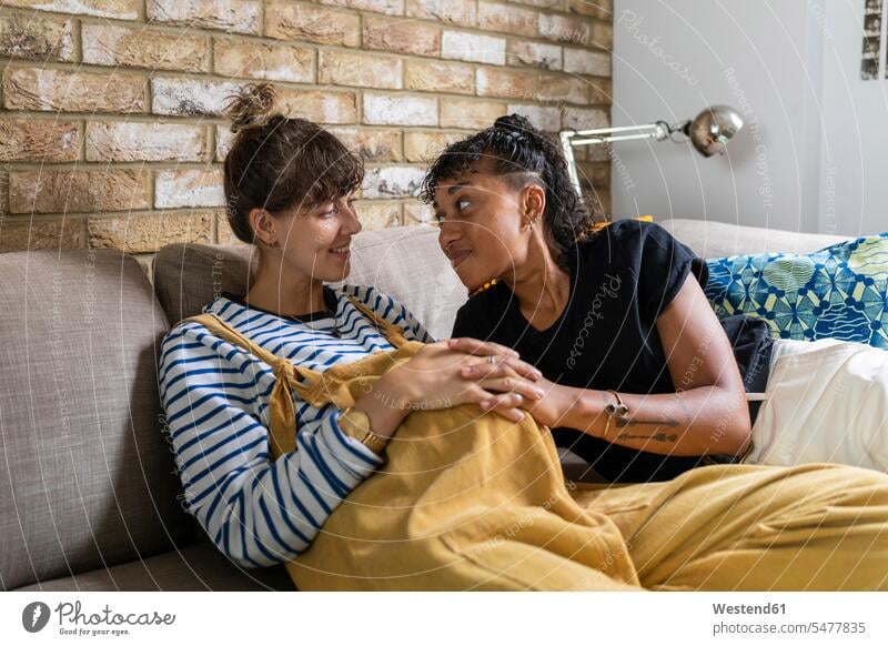 Smiling lesbian couple sitting with hands clasped on sofa at home color image colour image indoors indoor shot indoor shots interior interior view Interiors day