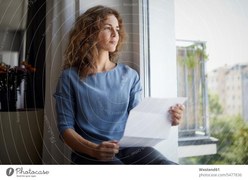 Woman holding paper while sitting on window sill at home color image colour image indoors indoor shot indoor shots interior interior view Interiors day