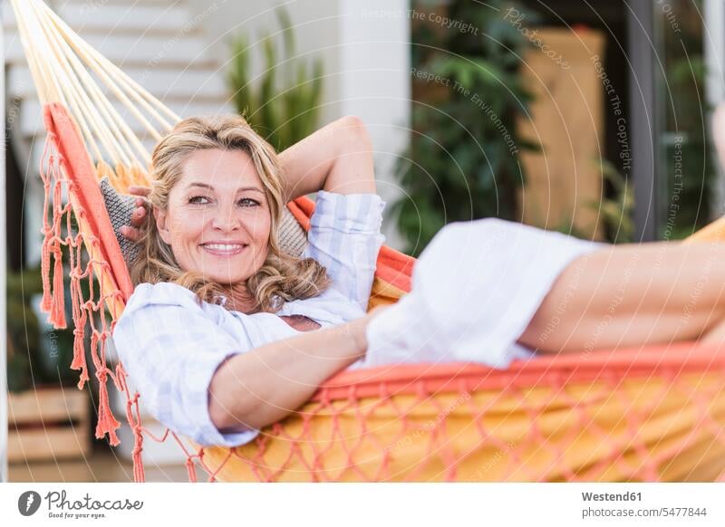 Portrait of smiling mature woman relaxing in hammock on terrace hammocks smile delight enjoyment Pleasant pleasure happy laying down lie lying down at home