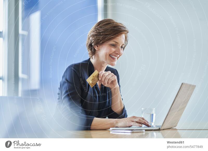 Smiling businesswoman holding credit card and using laptop at desk in office Occupation Work job jobs profession professional occupation business life