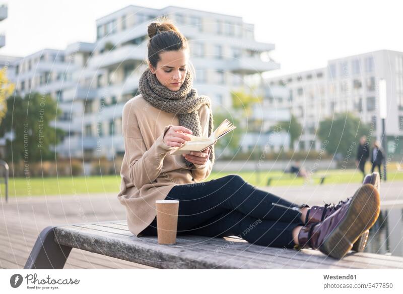 Woman with coffee to go sitting on bench in autumn reading a book fall woman females women books Coffee Seated benches Adults grown-ups grownups adult people