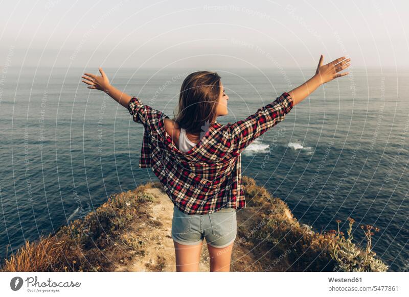 Young woman standing with arms outstretched against sea color image colour image outdoors location shots outdoor shot outdoor shots day daylight shot