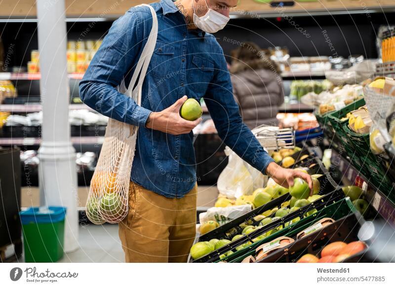 Midsection of man wearing face mask buying granny smith apples in supermarket color image colour image Spain leisure activity leisure activities free time