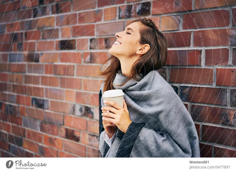 Happy woman with coffee to go in front of brick wall Coffee females women happiness happy brick walls Coffee to Go takeaway coffee Drink beverages Drinks