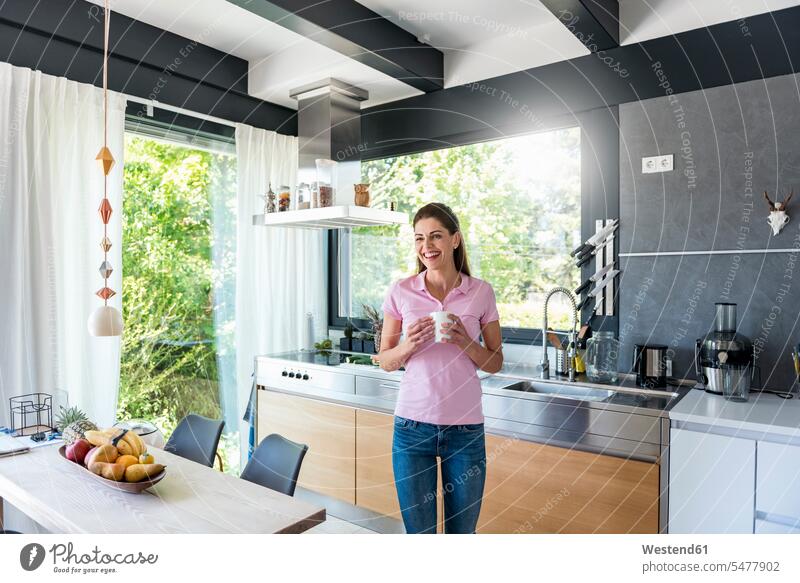 Laughing woman at home in kitchen with cup of coffee Coffee Coffee Cup Coffee Cups females women Drink beverages Drinks Beverage food and drink Nutrition