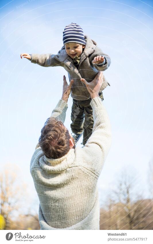 Father throwing happy boy in the air under blue sky happiness park parks father fathers daddy dads papa son sons manchild manchildren parents family families