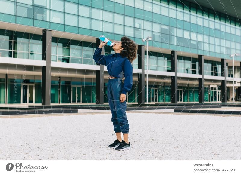 Sporty young woman having a cooling break in front of modern building human human being human beings humans person persons curl curled curls curly hair hold