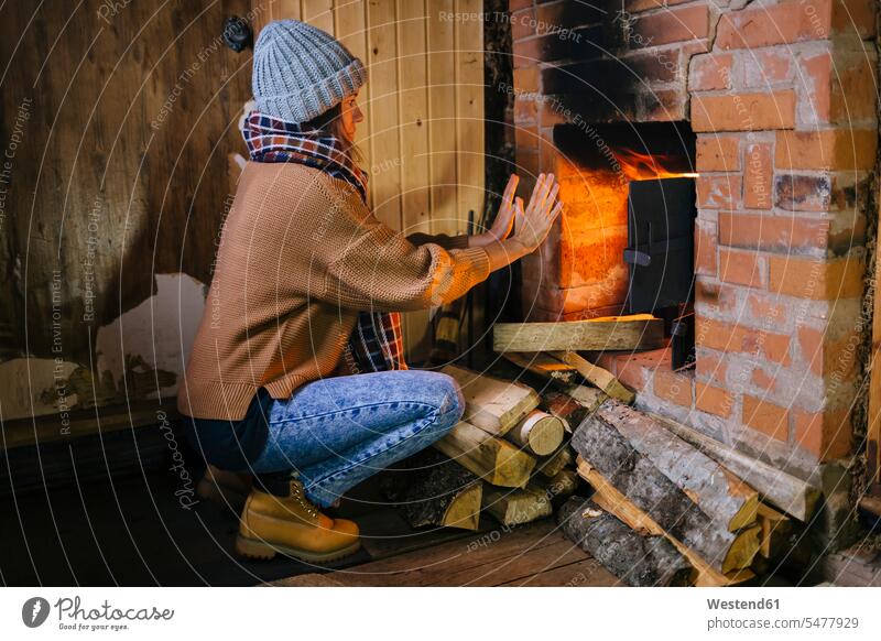 Woman crouching in front of fireplace warming her hands ovens scarfs scarves shine seasons hibernal at home Blaze free time leisure time comfortable cosy
