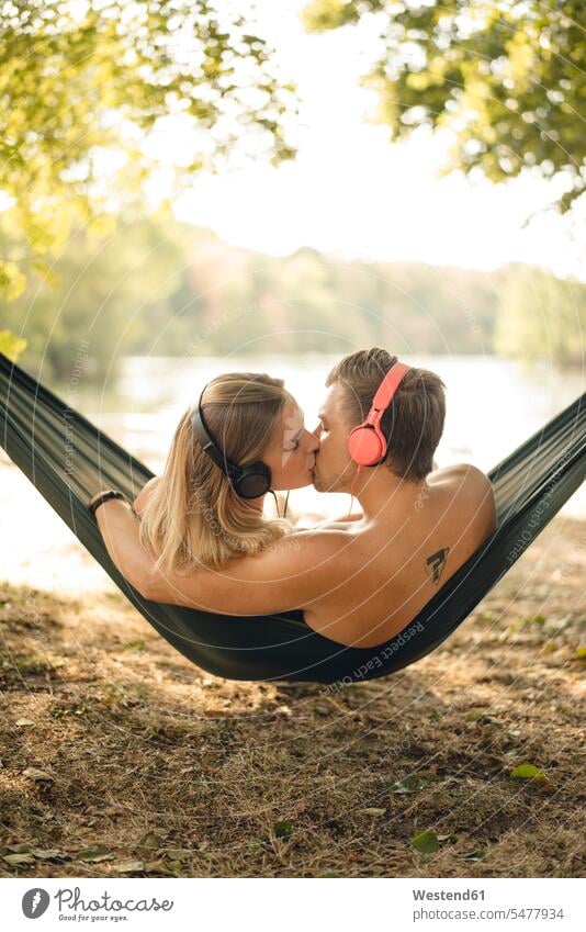 Couple relaxing in hammock by the lake, kissing, listening music human human being human beings humans person persons caucasian appearance caucasian ethnicity