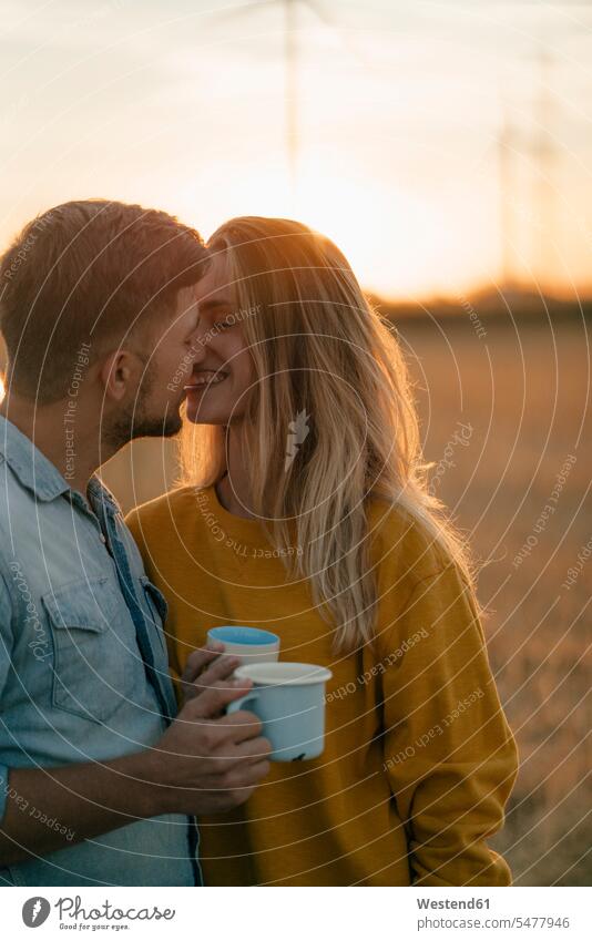 Happy young couple holding mugs kissing in rural landscape cup landscapes scenery terrain country countryside happiness happy twosomes partnership couples