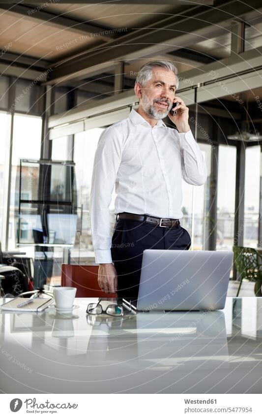 Businessman on cell pohone at desk in office offices office room office rooms Business man Businessmen Business men desks mobile phone mobiles mobile phones