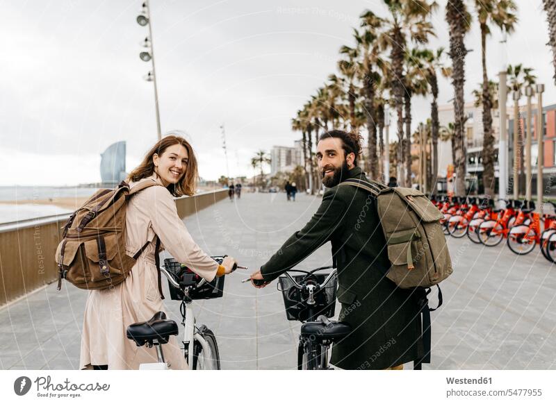 Smiling couple with e-bikes on beach promenade sea front boardwalk E-Bike Electric bicycle Electric Bike smiling smile twosomes partnership couples bicycles