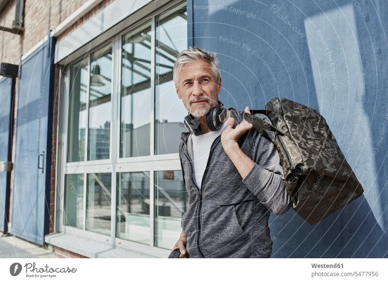 Portrait of mature man with headphones and camouflage sports bag in front of gym headset portrait portraits men males gyms Health Club Gym Bag Adults grown-ups
