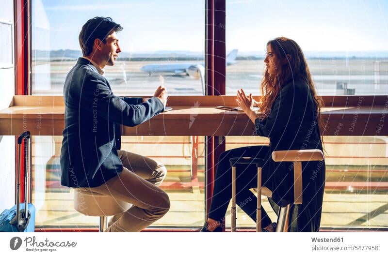 Business couple talking while sitting at airport cafe color image colour image indoors indoor shot indoor shots interior interior view Interiors day