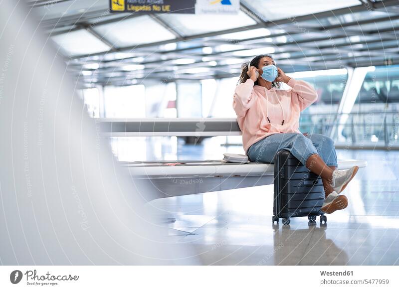 Young woman listening to music while wearing protective face mask sitting at airport color image colour image indoors indoor shot indoor shots interior