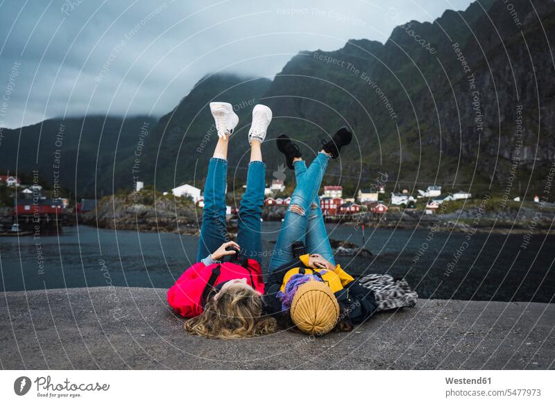 Norway, Lofoten, two young women lying on a pier at the coast woman females piers coastline shoreline laying down lie lying down Adults grown-ups grownups adult