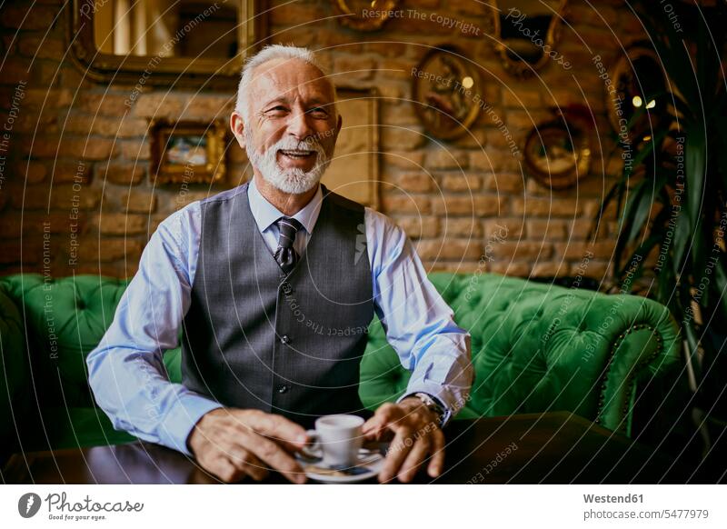 Portrait of elegant senior man sitting on couch in a cafe smiling portrait portraits settee sofa sofas couches settees men males smile chic elegance stylishly