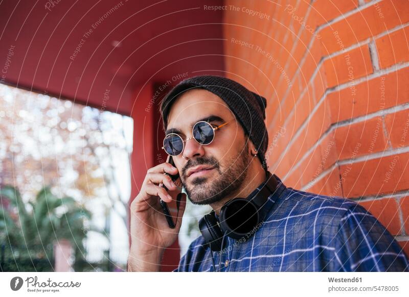 Fashionable young man wearing sunglasses on phone call against brick wall color image colour image outdoors location shots outdoor shot outdoor shots day