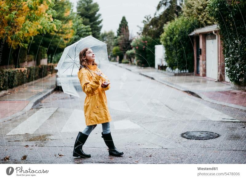 Smiling girl in raincoat holding umbrella while walking on road in city color image colour image day daylight shot daylight shots day shots daytime Spain
