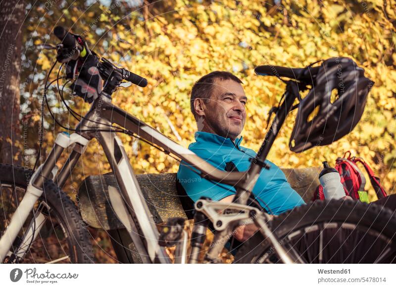 Man with mountainbike having a break sitting on a bench Seated man men males mountain bike benches forest woods forests Adults grown-ups grownups adult people