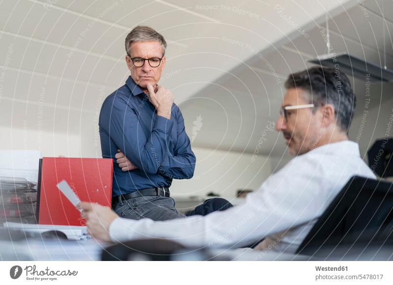 Mature male coworkers discussing over document while sitting in office color image colour image Germany indoors indoor shot indoor shots interior interior view