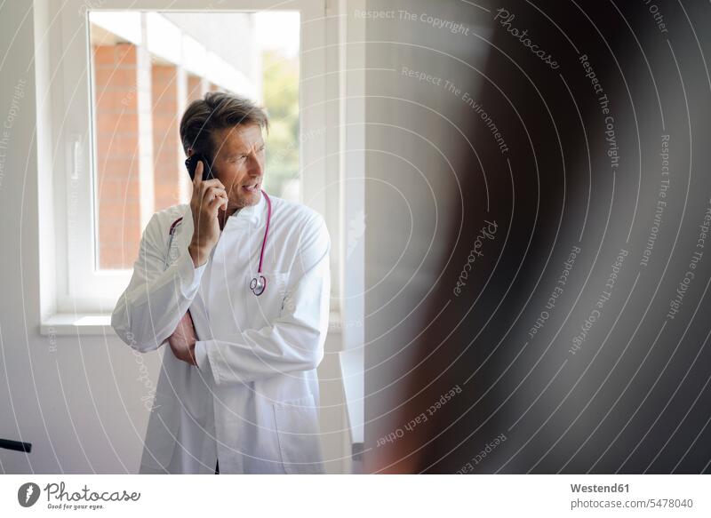 Doctor standing in hospital, using smartphone doctor's overall lab coat Smartphone iPhone Smartphones stethoscope physicians doctors portrait portraits